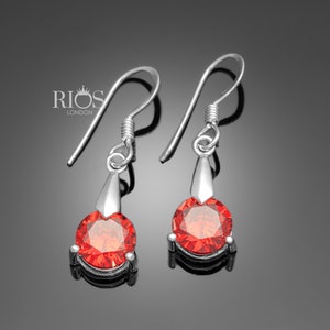 May include: A pair of silver dangle earrings with red round gemstones. The earrings have a simple design with a small drop.