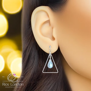 Puede incluir: Pendientes de plata de forma triangular con una piedra preciosa azul en forma de lágrima que cuelga de la parte inferior.