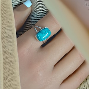 May include: A silver ring featuring a turquoise gemstone. The ring is worn on a finger.