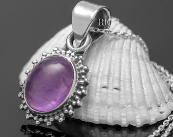 Könnte beinhalten: Ein silberner Anhänger mit einem violetten Amethyst-Edelstein, der in einem Sternburst-Design gefasst ist. Der Anhänger liegt auf einer weißen Muschel.