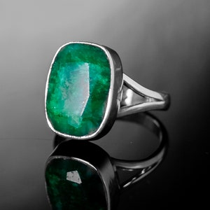 May include: A silver ring featuring a large, emerald green gemstone. The gemstone is set in a bezel setting and the ring has a simple, elegant design.