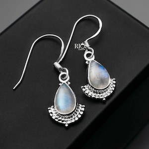 May include: A pair of silver dangle earrings featuring a teardrop-shaped moonstone gemstone and a silver filigree design. The earrings are displayed against a black background.