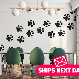May include: Black paw print wall decals arranged in a diagonal pattern on a white wall. The decals are in a dining room setting with a table and chairs.