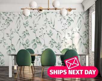 May include: A white wall with a green watercolor floral pattern. The wall is behind a dining table with four green chairs. The table is white and has a gold metal chandelier hanging above it.