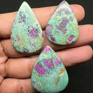 May include: Three teardrop-shaped gemstones with a turquoise matrix and vibrant magenta inclusions. The stones are polished, showcasing a mix of colors and textures. The gemstones are likely for jewelry making.