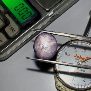 May include: A close-up of a purple gemstone with a white star-like pattern, being measured with a gem gauge. The gauge reads 0.1mm and 20mm.