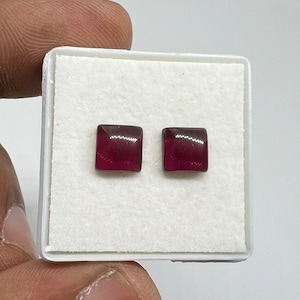 Puede incluir: Un par de pendientes de forma cuadrada con una piedra preciosa de color rojo intenso.