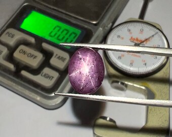 Pode incluir: Uma gema de safira estrela púrpura com uma estrela de seis pontas no centro. A gema está sendo medida com um paquímetro e uma balança.