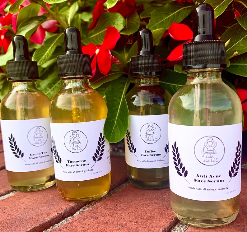 K&ouml;nnte beinhalten: Vier Glasflaschen mit Tropfern, die Gesichts Seren enthalten. Die Flaschen sind mit den Namen der Seren beschriftet: Green Tea Face Serum, Turmeric Face Serum, Coffee Face Serum und Anti Acne Face Serum. Jede Flasche ist mit dem Markennamen "Smooth Like Jas, LLC" beschriftet.