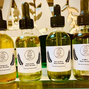 K&ouml;nnte beinhalten: Vier Glasflaschen mit Tropfern, die Gesichts Seren enthalten. Die Flaschen sind mit den Namen der Seren beschriftet: Kurkuma Gesichts Serum, Anti Akne Gesichts Serum, Gr&uuml;ner Tee Gesichts Serum und Kaffee Gesichts Serum. Jede Flasche hat ein wei&szlig;es Etikett mit schwarzem Text und einer kleinen Illustration einer Person mit einem Heiligenschein.