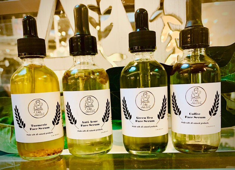 K&ouml;nnte beinhalten: Vier Glasflaschen mit Tropfern, die Gesichts Seren enthalten. Die Flaschen sind mit den Namen der Seren beschriftet: Kurkuma Gesichts Serum, Anti Akne Gesichts Serum, Gr&uuml;ner Tee Gesichts Serum und Kaffee Gesichts Serum. Jede Flasche hat ein wei&szlig;es Etikett mit schwarzem Text und einer kleinen Illustration einer Person mit einem Heiligenschein.