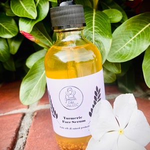 K&ouml;nnte beinhalten: Eine durchsichtige Glasflasche mit einer Tropfpipette, gef&uuml;llt mit einer gelben Fl&uuml;ssigkeit. Die Flasche hat ein wei&szlig;es Etikett mit schwarzem Text, auf dem "Smooth Like Jas, LLC" und "Turmeric Face Serum" steht, darunter die Worte "Made with all natural products". Die Flasche steht auf einer Ziegelstein-Oberfl&auml;che mit einer wei&szlig;en Blume.