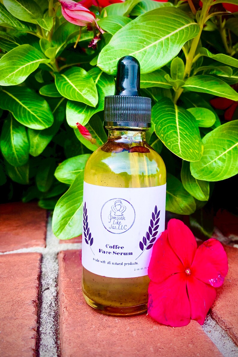 K&ouml;nnte beinhalten: Eine durchsichtige Glasflasche mit schwarzem Tropfer und einem wei&szlig;en Etikett. Das Etikett tr&auml;gt die Aufschrift "Smooth Like Jas, LLC" und "Coffee Face Serum". Die Flasche steht auf einer Ziegelstein-Oberfl&auml;che mit einer rosa Blume.