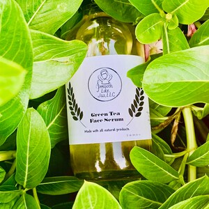 K&ouml;nnte beinhalten: Eine durchsichtige Glasflasche mit einem wei&szlig;en Etikett, auf dem "Green Tea Face Serum" und "Made with all natural products." steht. Die Flasche ist von gr&uuml;nen Bl&auml;ttern umgeben.