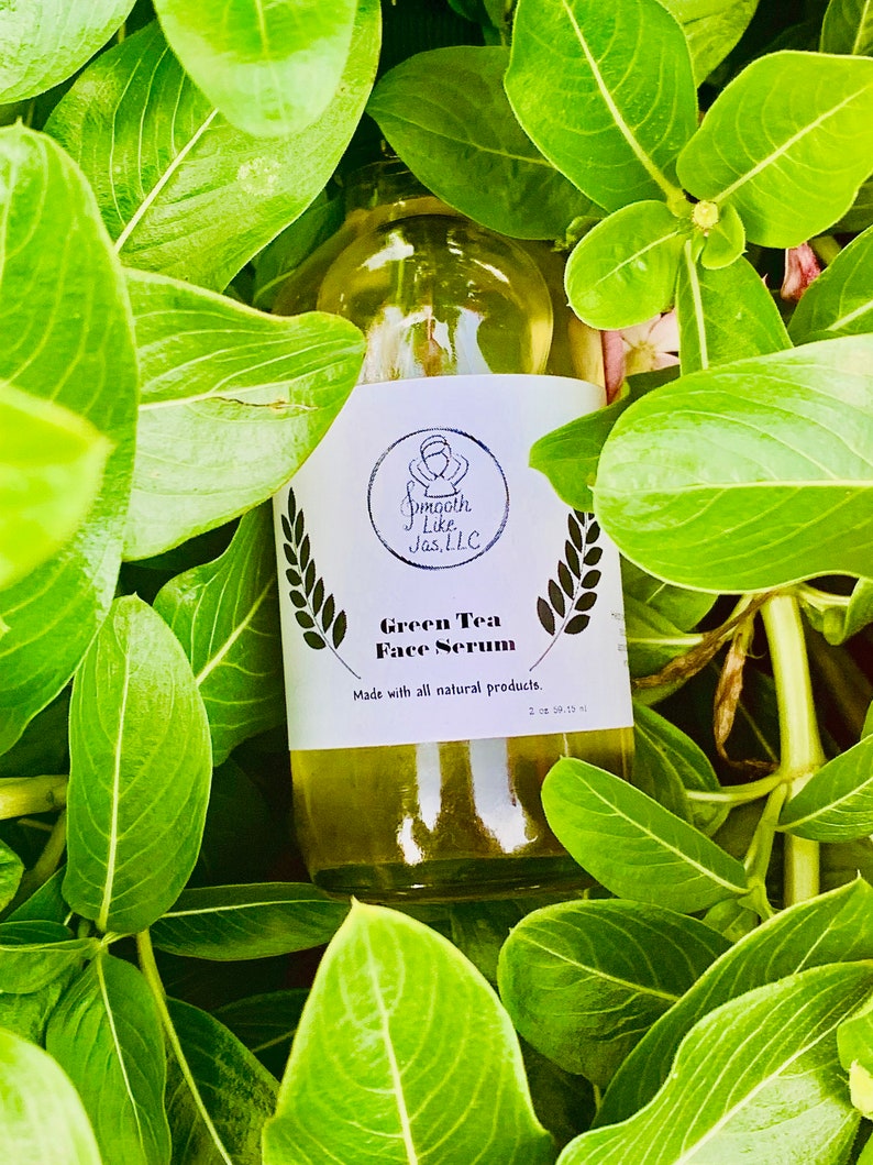 K&ouml;nnte beinhalten: Eine durchsichtige Glasflasche mit einem wei&szlig;en Etikett, auf dem "Green Tea Face Serum" und "Made with all natural products." steht. Die Flasche ist von gr&uuml;nen Bl&auml;ttern umgeben.