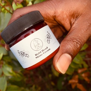 May include: A brown jar with a black lid and a white label that says "Smooth Like Jaslic" and "Bald Head Shine Cream".
