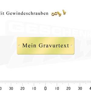 May include: A gold-colored metal plaque with the text "Mein Gravurtext" and two small holes for mounting. The plaque is shown with screws for mounting.