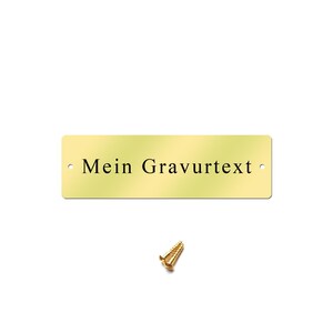 May include: A gold-colored metal plaque with rounded corners and two holes for hanging. The plaque has the text "Mein Gravurtext" engraved on it. A small gold screw is included.