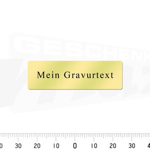 May include: A gold-colored rectangular nameplate with the text "Mein Gravurtext" in black.