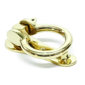 Könnte beinhalten: Ein polierter Türklopfer aus Messing mit einem runden Ring und einem rechteckigen Sockel.