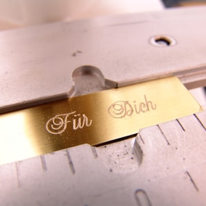 May include: A gold-colored metal plate with the words "F&uuml;r Dich" engraved in a cursive font.