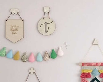 May include: A pink wall with a variety of wall decor, including a woven wall hanging with pink, yellow, and blue tassels, a banner that reads "NORMAL IS BORING" in rainbow letters, and a framed print that says "HELLO" in colorful letters.