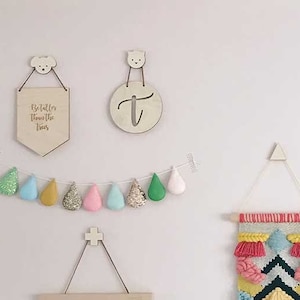 May include: A pink wall with a variety of wall decor, including a woven wall hanging with pink, yellow, and blue tassels, a banner that reads "NORMAL IS BORING" in rainbow letters, and a framed print that says "HELLO" in colorful letters.