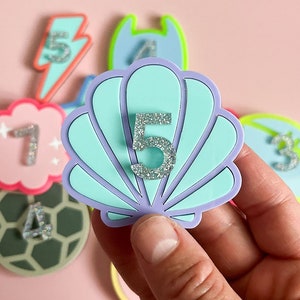 Peut inclure: Un ensemble de patchs en feutre colorés avec les chiffres de 1 à 5. Le chiffre 5 est sur un patch en forme de coquille de couleur bleu clair.