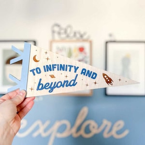 May include: A wooden pennant with a blue and white design. It says "To Infinity and Beyond" with a crescent moon, stars, and a rocket ship.