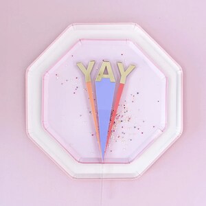 May include: Three pink and white paper plates with a gold "YAY" topper in the center. The topper is on a clear plastic stick.