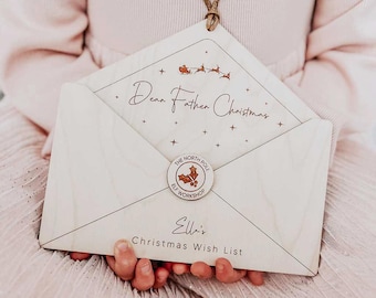 May include: A wooden Christmas wish list shaped like an envelope, held by a child. The envelope reads "Dear Father Christmas" with a reindeer and sleigh illustration. It also features a "The North Pole Elf Workshop" sticker and the name "Ella's Christmas Wish List."
