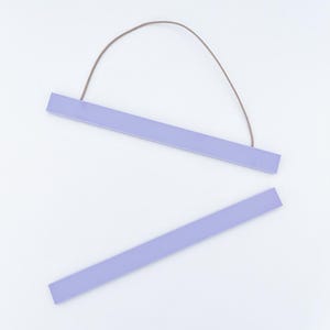 Peut inclure: Deux cintres en bois de couleur lavande pour affiches. Le cintre supérieur est muni d'une ficelle marron pour l'accrochage. Le cintre inférieur est séparé. Les cintres sont rectangulaires et ont une finition lisse. Le fond est blanc.