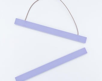 May include: A set of two lavender-colored wooden poster hangers. The top hanger has a brown string attached for hanging. The bottom hanger is separate. The hangers are rectangular and have a smooth finish. The background is white.