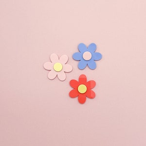 May include: Three paper flowers with a pink, blue, and red background. The flowers have yellow centers.