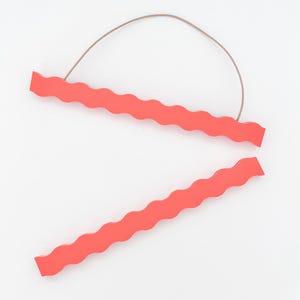 May include: Two coral-coloured wooden poster hangers with a wavy edge design. The top hanger has a thin, brown string attached for hanging. The hangers are displayed against a white background.