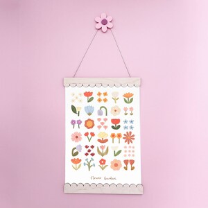 May include: A white print with a scalloped wooden frame hangs on a pink wall. The print features a colorful illustration of various flowers with the text "Flower Garden".