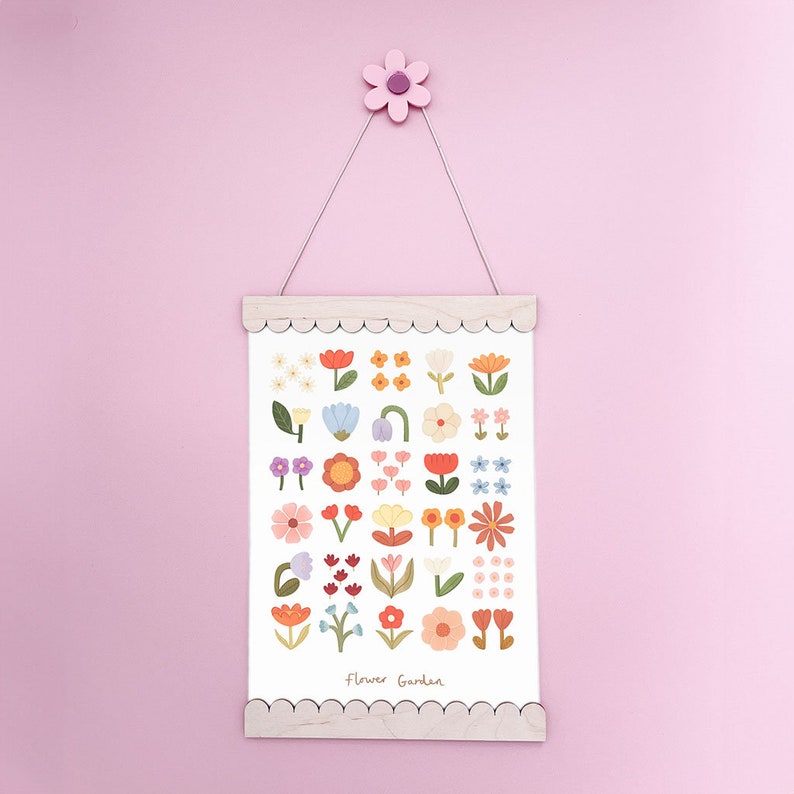 May include: A white print with a scalloped wooden frame hangs on a pink wall. The print features a colorful illustration of various flowers with the text "Flower Garden".