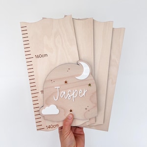 May include: Wooden growth chart with a decorative nameplate. The nameplate features a moon, stars, and the name "Jasper" in white. The chart measures up to 160cm (63 inches).