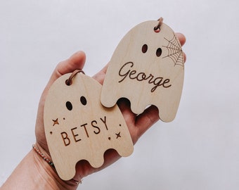 May include: Two wooden ghost ornaments with the names "Betsy" and "George" engraved on them. The ghost with the name "George" has a spiderweb design on it.