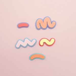 Puede incluir: Cinco formas abstractas de colores hechas de papel, incluyendo una línea ondulada, un garabato, una línea curva y dos garabatos. Las formas están sobre un fondo rosa.