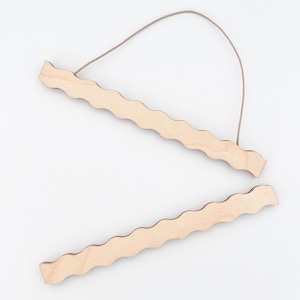 May include: Two unfinished wooden poster hangers with a wavy edge design. The top hanger has a brown string attached for hanging. The wood has a natural, light color. The hangers are designed to hold posters or artwork.