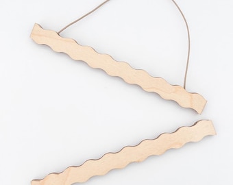 May include: Two unfinished wooden poster hangers with a wavy edge design. The top hanger has a brown string attached for hanging. The wood has a natural, light color. The hangers are designed to hold posters or artwork.