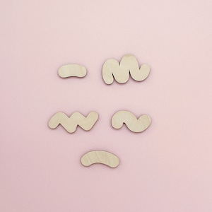May include: Five wooden shapes in various abstract forms, including wavy lines, curves, and a rounded rectangle, arranged on a light pink background.