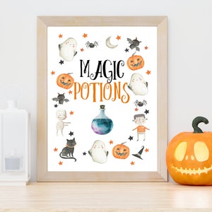 May include: A framed print with the words "MAGIC POTIONS" surrounded by Halloween-themed illustrations. The illustrations include pumpkins, ghosts, bats, spiders, and a potion bottle. The frame is light brown.