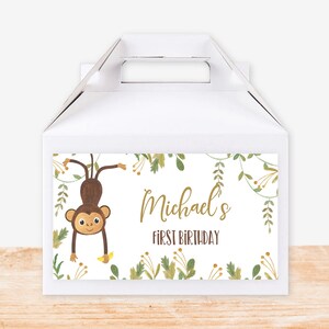 Pode incluir: Caixa de favor branca com tema de selva verde e marrom. A caixa tem um macaco pendurado em uma videira e o texto "Michael's First Birthday".