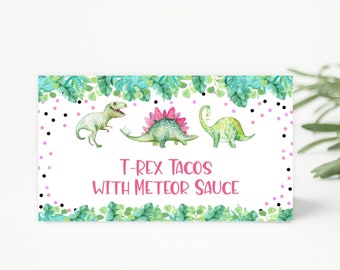 Puede incluir: Una etiqueta de comida imprimible con fondo blanco y hojas verdes alrededor del borde. La etiqueta tiene lunares rosas y negros y tres dinosaurios de dibujos animados. El texto dice "T-Rex Tacos with Meteor Sauce".