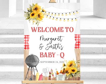 Op de afbeelding: Welkom bij Margaret & Smith's Baby-Q, een rustiek welkomstschild met zonnebloemen, lichtslingers en een barbecue, op een houten ezel geplaatst. De datum 24 september 2020 staat op het bord gedrukt.
