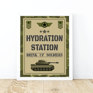 Könnte beinhalten: Ein Schild mit grünem und braunem Tarnmuster mit dem Text "Hydration Station" und "Drink Up Soldiers". Unter dem Text befindet sich ein Cartoon-Panzer.