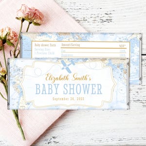 May include: A blue and white baby shower chocolate bar wrapper with a map design and a gold airplane. The text on the wrapper reads "Elizabeth Smith's Baby Shower September 24, 2013".