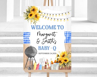 Op de afbeelding: Een houten bord met de tekst "WELCOME TO Margaret & Smith's BABY-Q" in blauw en zwart. Het bord toont een barbecue, zonnebloemen en lichtslingers, met de datum "SEPTEMBER 24, 2020" onderaan.